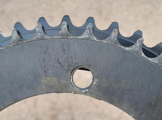 Closeup photo of two bike chain rings. The one below is new and the other on top is very worn out.