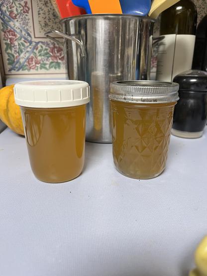 A photo of two half-pint jars of slightly cloudy amber-colored syrup, on a kitchen counter. One jar has a screw-on plastic lid, the other has a vacuum heat-sealed canning lid.