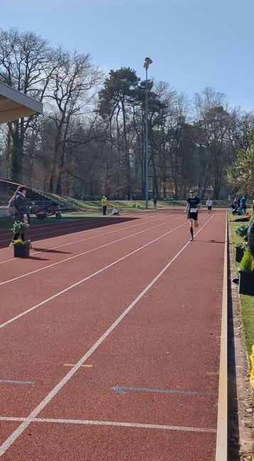 Die Tartanbahn eines Leichtathletik-Stadions, auf Bahn 1 befinde ich mich im Zieleinlauf. Im Hintergrund die Bäume des Bienwalds, auf der linken Seite die Ausläufer einer Tribüne.