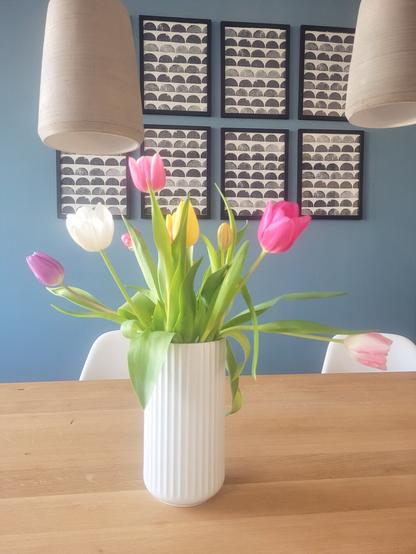 DEU Vor einer blau gestrichenen Wand steht auf einem Holztisch eine weiße Vase mit bunten Tulpen

ENG A vase filled with colourful tulips on a wooden table in front of a petrol blue wall