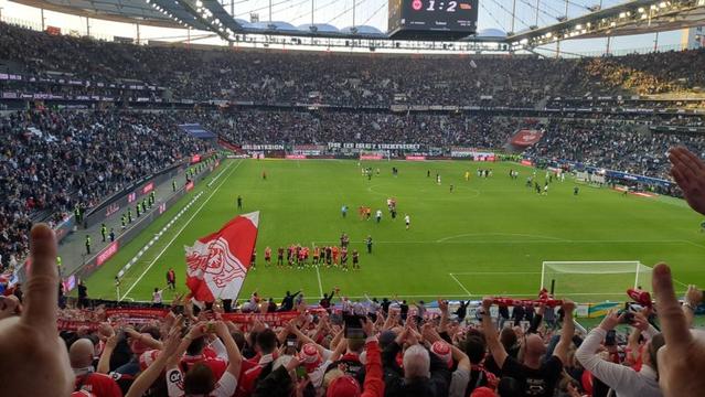 Blick von Union Fans ins Waldstadion. Das jubelnde Team auf dem Rasen vor der Fankurve. Oben der Endstand Frankfurt 1 Union 2