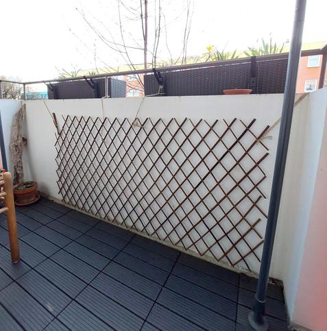 Die lange Innenseite des Balkons ist mit einem Rankgerüst aus Weidenholz verkleidet. Rechts vom Gerüst steht eine Stange der Markise.