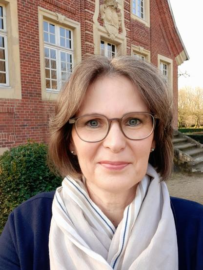 Frau mit braunen Haaren und Brille vor einem Baxksteingebäude, Rüschhaus im Münsterland
