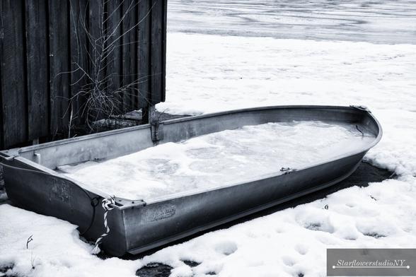 A metal row boat filled with ice on the beach.  Black and white photo.