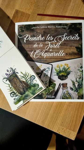 English On a wooden table are a book entitled Paint the secrets of the forest with watercolor (in French) by Jennifer Lefèvre @jenny_illustrations, published by Eyrolles, and a notebook with a watercolor depicting a tree stump amid ferns with purple mushrooms growing on it.
Français Sur une table en bois sont posés un livre intitulé Peindre les secrets de la forêt à l'aquarelle de Jennifer Lefèvre @jenny_illustrations aux éditions Eyrolles et un carnet avec une aquarelle représentant une souche d'arbre au milieu des fougères avec des champignons violets qui poussent dessus.