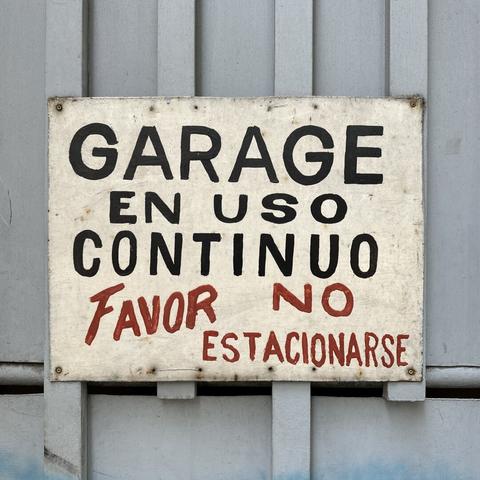 A handpainted sign in black and red lettering: “Garage en uso continuo, Favor no estacionarse.”