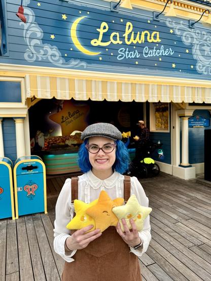 Woman wearing a pair of brown overalls and a hat holding 3 star plushies
