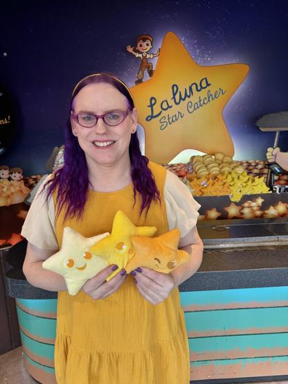 Woman wearing a bright yellow dress and holding 3 star plushies