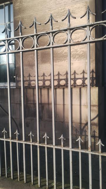 Railings with arrowhead tops, and their shadows cast onto stone wall behind them