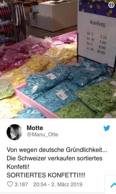 Farbig sortierte Konfettisäcke in der Schweiz, worüber sich ein deutsches Posting im Internet etwas lustig macht, es aber eigentlich einen sehr guten Grund dfür gibt. / A colorful display of confetti bags in various colors, including pink, yellow, blue, and green, is shown on a table. A sign indicates the prices for different sizes. The accompanying text humorously remarks on the organized nature of Swiss confetti