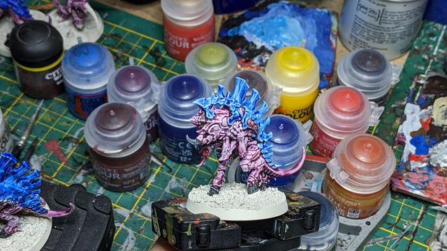 A Tyranid with a big gun painted in blue and purple. In the background you can see many paint pots.
