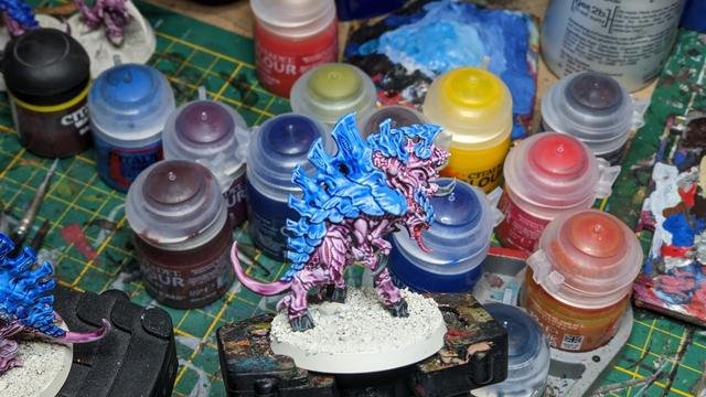 A Tyranid with a big gun from the other side painted in blue and purple. In the background you can see many paint pots.