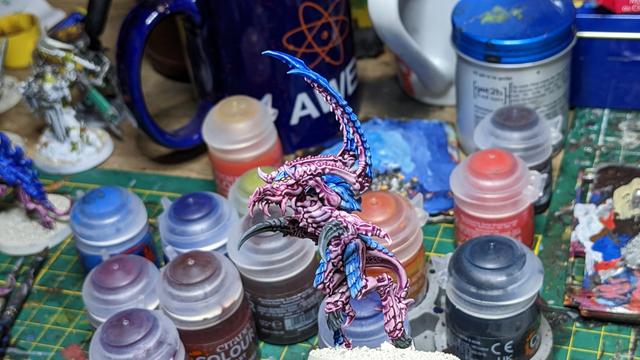 A Tyranid with big claws painted in blue and purple. In the background you can see many paint pots.