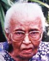 Latifah Bee Ghows, late in life; an old woman with brown skin and white hair, wearing glasses and a print top, photographed outdoors