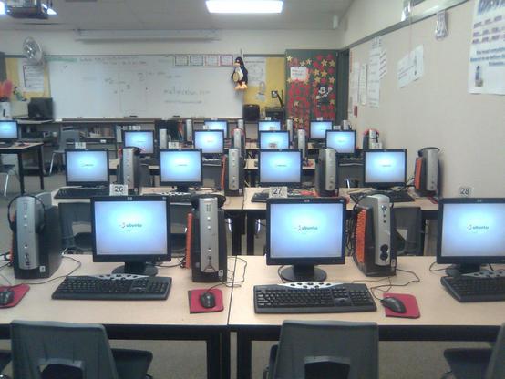 An elementary school's computer lab, with rows of computers booted up to Ubuntu LTSP. A stuffie of Tux is hanging on the front whiteboard.