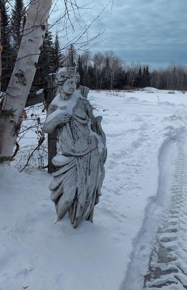 A grey statue guards the entrance to a snowy field