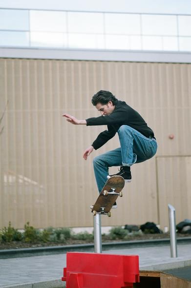 Skateboarder in black shirt and blue jeans jumpingva red obstacle