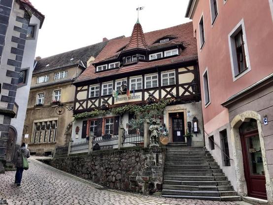 Here is a concise description of the image:

"This picture shows an old building with half-timbered walls and a red roof, situated on a cobblestone street lined with other historic buildings. The building features multiple windows and a sign that reads "Jürgens Nachtigall" in German script."