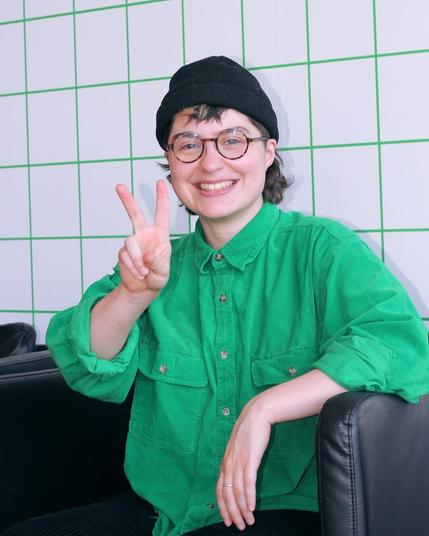 Portrait of me smiling in a bright green corduroy shirt making the peace sign.