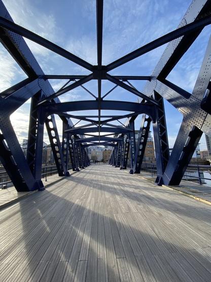 A view looking back down the Victoria Swing Bridge in Leith, Scotland. The wooden surface of the bridge and blue metal structure are visible. No-one is visible on the bridge.