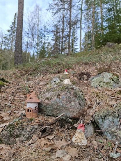 Keraamisia tonttuja ja mökkejä kivikossa metsän laidassa.