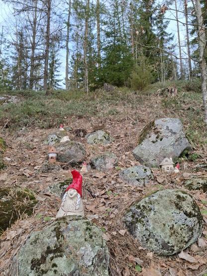 Keraamisia tonttuja ja mökkejä kivikossa metsän laidalla.