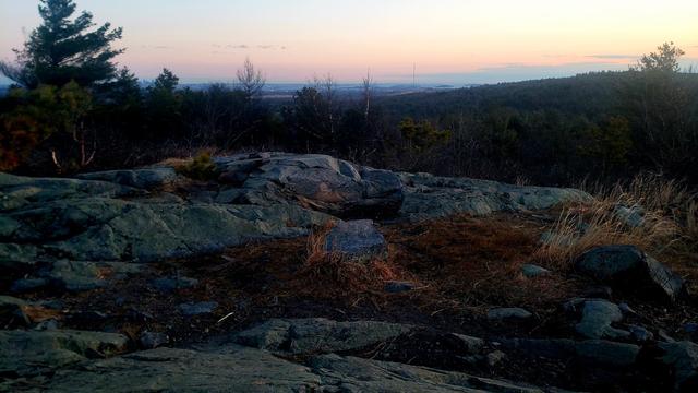 The blue rock at the summit of Buck Hill catches the dawn light. Boston Harbor can be seen on the horizon.