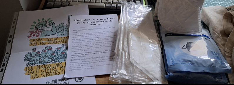 Photographie avec la préparation du matériel : une affiche de Winslow Santé Public, une brochure Réutilisation d'un masque FFP2, des masques bec de canard blanc texinov, un pack de 5 masques noir cameron davis, et un masque blanc en sachet individuel