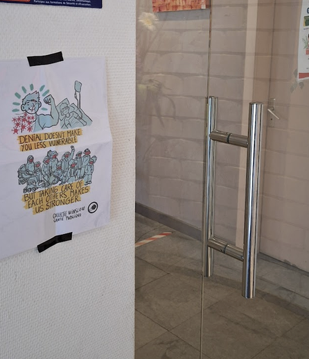 Une photo de l'entrée du laboratoire, avec l'affiche de Winslow Santé publique scotché avant la porte,
L'affiche est dessinée par Calvinarium
Il est écrit en anglais : Le déni ne te rend pas moins vulnérable mais prendre soin les unEs des autres nous rend plus fortEs.