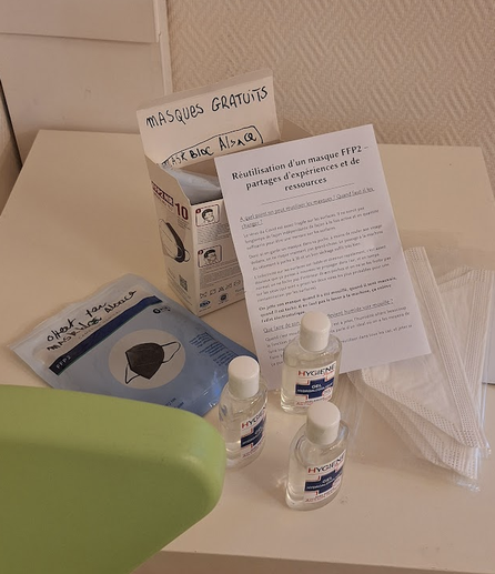 Une photographie d'une table basse sur laquelle sont posées les masques, une boîte et la brochure
C'est inscrit Masques gratuits et masques offert par Mask Bloc Alsace
Il y a également des tubes de gels hydroalcooliques.