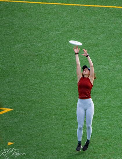 A woman with a look of determination stretches into the air at a park to catch a frisbee.