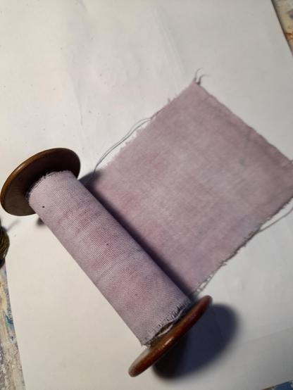 A large dark brown wooden spool with the purple fabric wound onto it. The antique bobbins come from old weaving mills. Dyed with red tea and fixed with salt, the fabric gets an interesting degraded colouring of blueish purple.