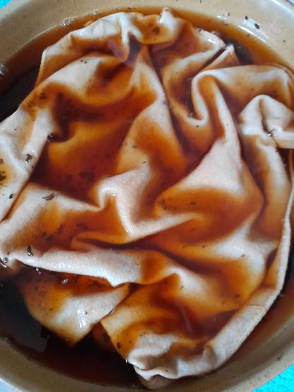 Some of the white fabric in concentrated black tea. In a hot tea bath, after some hours, the fabric will be dyed in natural colours.