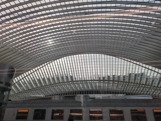 a modern take on the open and clear glass train shed roof at Liège, with bidirectional curvature and lighter-weight grey arches, no columns in the interior space