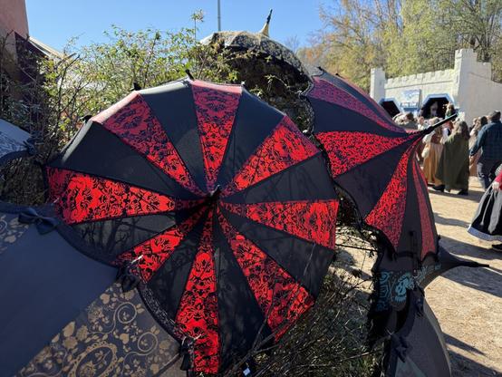 Elegant black and red lace parasols with intricate patterns on display at a Renaissance Festival, with a lively crowd in the background.