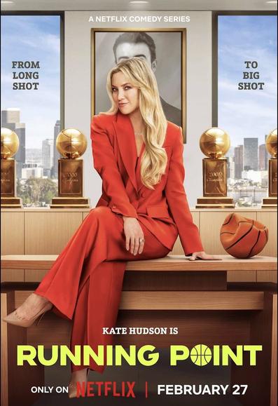 Kate Hudson in a bright red suit perches on the edge of a desk. Beside her is a deflated basketball.
