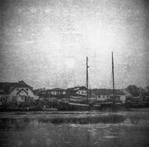 Black and white photo, 6x6. A sailing ship lies in an icy harbour. The expired film leads to the image of the protective paper on the emulsion. This makes the photo look as if it is very old.