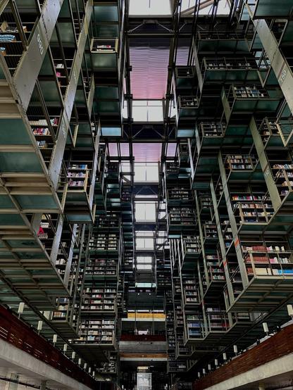Looking up from the main floor at vast, translucent green shelving spanning multiple floors. Purple and pink light filters in across the ceiling.