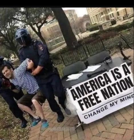 Image description:
Adapted meme:
Table and chair outside, it says “America is a free nation, change my mind”. The guy is not on his chair, people in black uniforms are carrying him away.