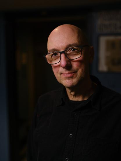 A man with a trace of a closed-mouth smile looks thoughtfully toward the camera