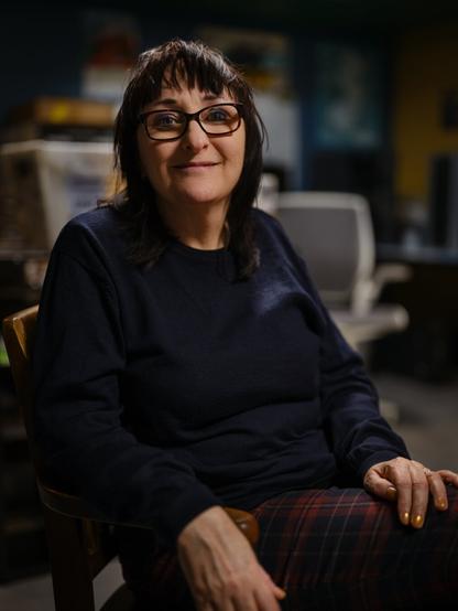 A woman in a chair looks toward the camera with a subtle smile.