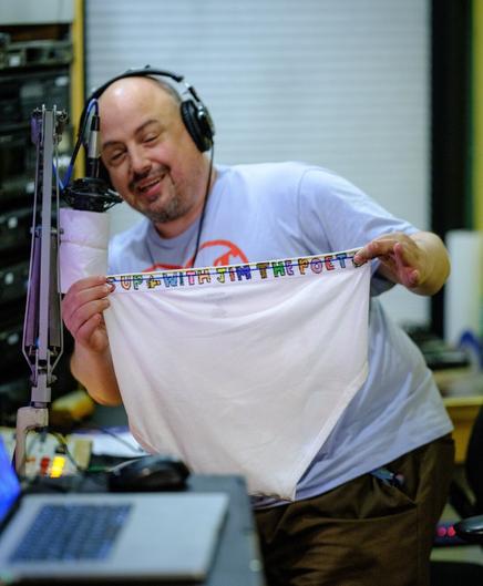 A man, his face not really in focus, holds up an enormous pair of white "tighty whitey" or "y-front" underpants with hand-decorated band