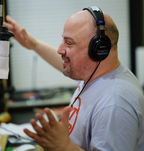 A man wearing headphones gesticulates.  His hands are blurry.