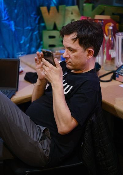 A man wearing a WFMU DEVO-style tee shirt reads his phone.