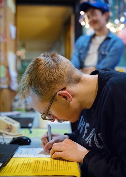 A man has his head very near a sheet of paper he's writing on.  He appears to be paying close attention to what he's doing.