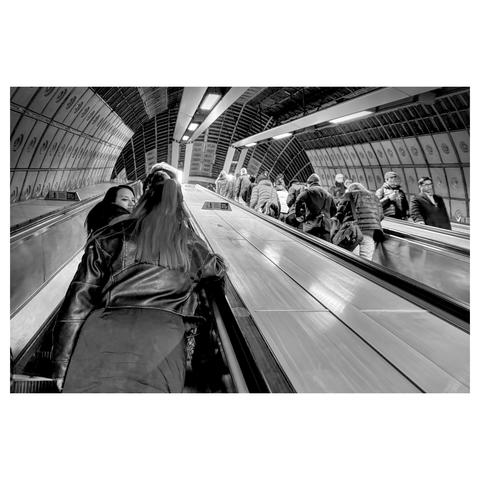 Black and white photo shot while travelling on an escalator showing other people on their way about the city of London