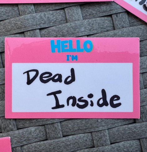 Pink sticker with blue text at the top that says "Hello I'm" with a white box below it with handwritten words "Dead Inside"