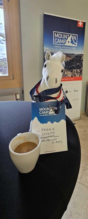 Franz Joseph, mascot of DrupalconVienna having a coffee at mountaincamp 2025