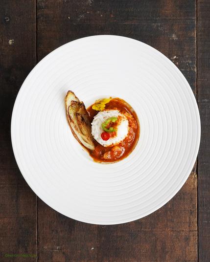 Dunkler Holzuntergrund. Darauf ein kleiner Pastateller (eigentlich ein Desserteller:-) Darin: »Geschmorter Chicorée mit Reis und einer Sauce mit selbstgemachtem Garam Masala«