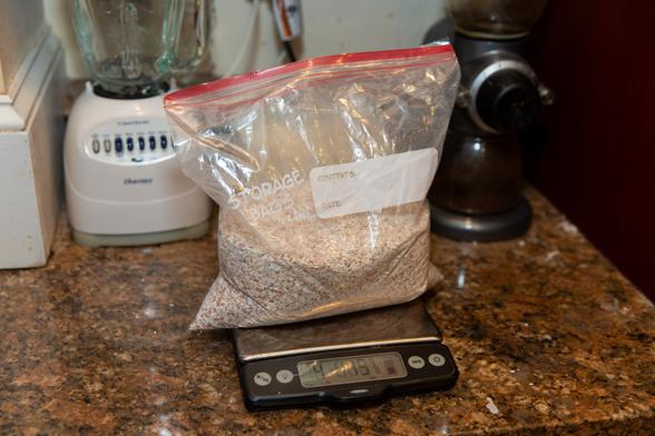 One-gallon ziploc bag filled with finely-ground brown eggshells, resting on a scale that reads, "4 lbs 15 7/8 oz."